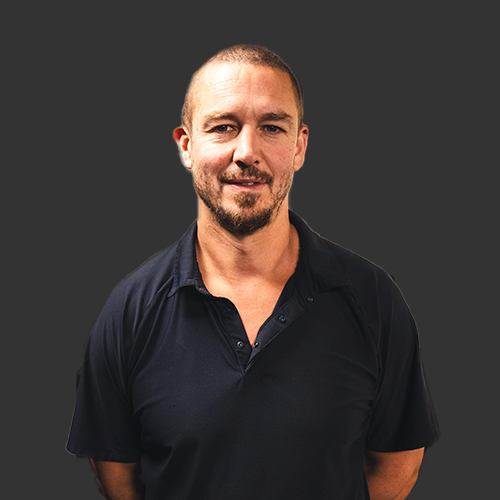 Olympic trainer Stuart White wearing a black collared shirt and hands behind his back, smiling.